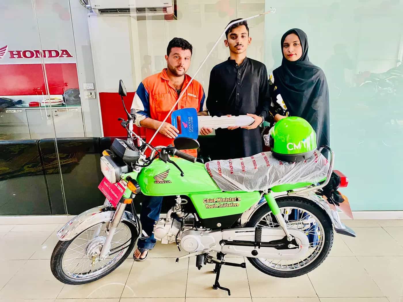 A brother and sister receiving the keys of their new green CM Youth Initiative bike at a Honda dealership