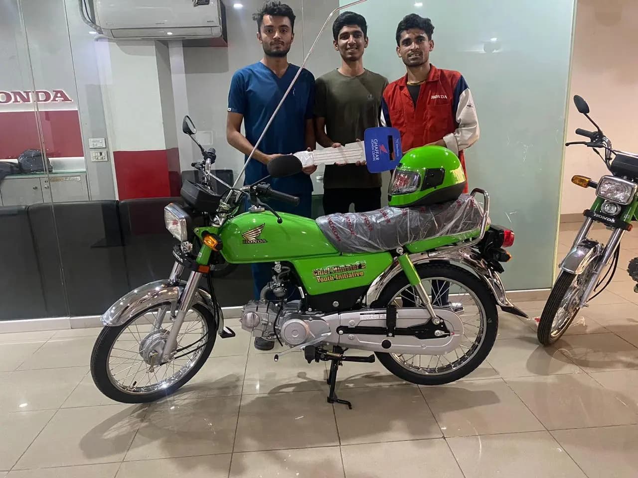 Three students with a new green CM Youth Initiative Honda bike